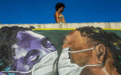Uma mulher vestindo uma máscara facial está acima de um grafite do artista brasileiro Marcos Costa, ou Spray Cabuloso, na entrada da favela Solar de Unhão, em Salvador, Bahia.